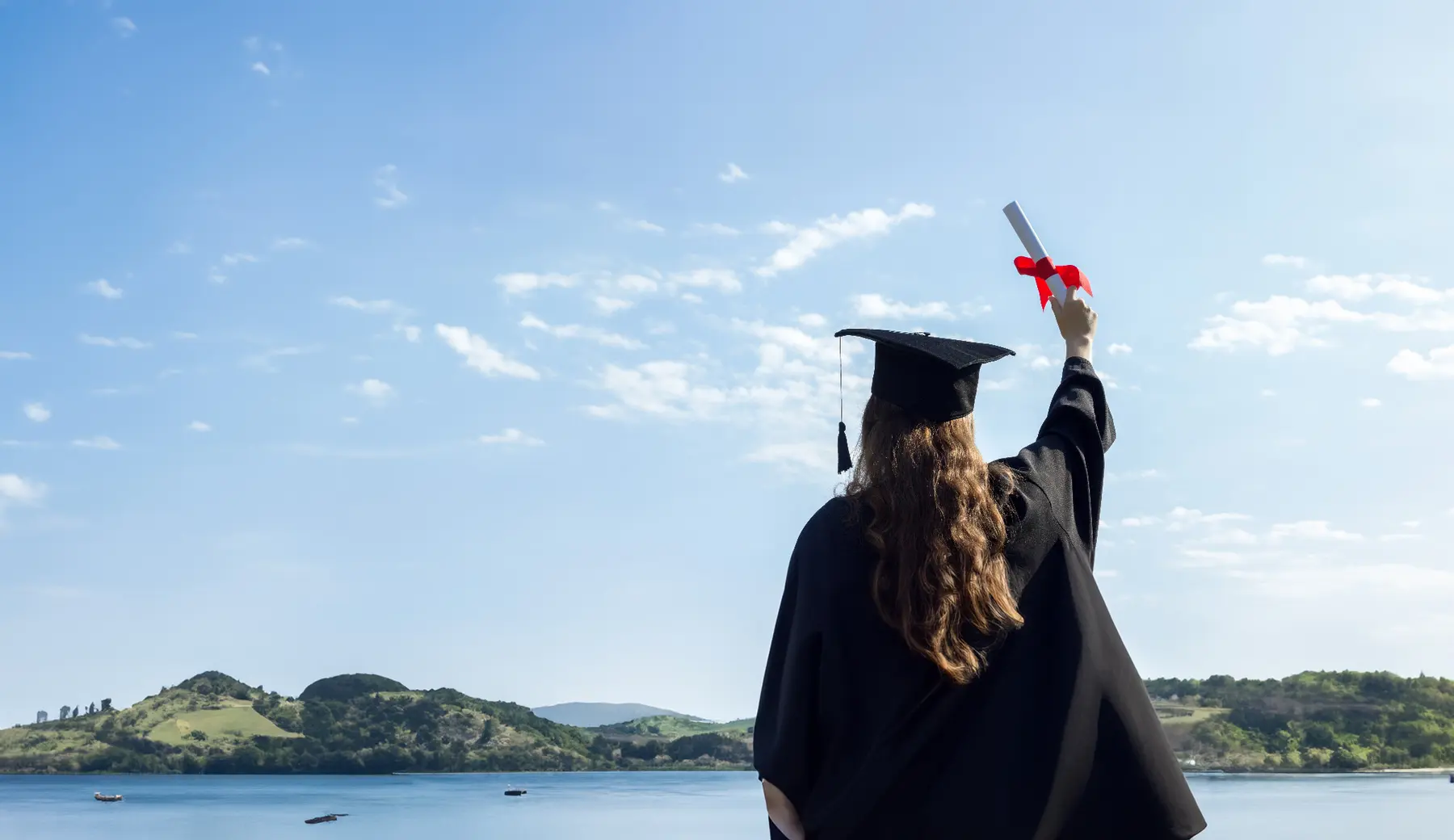 Graduate holding a diploma towards an open sky